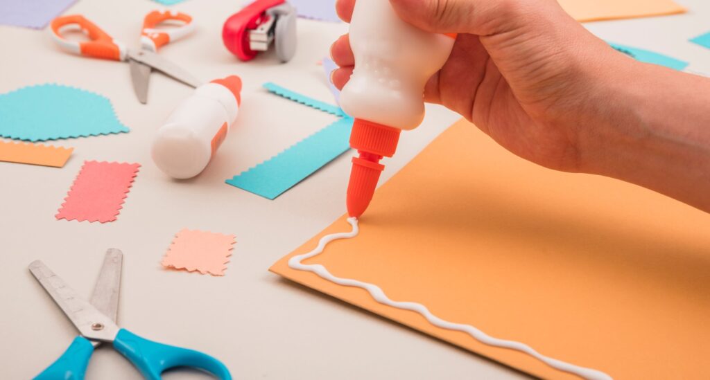 women hand applying clue on orange cardboard paper, remove glue from skin